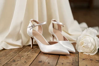 Escarpins blancs en satin pour mariage posés sur parquet en bois avec robe de mariée et bouquet de pivoines