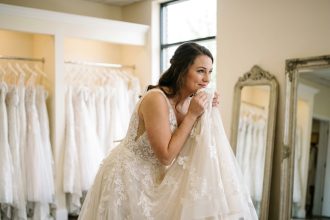Jeune femme essayant une robe de mariée ivoire élégante dans une boutique de mariage avec des robes en arrière-plan